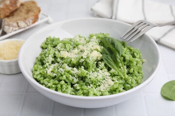 Delicious spinach risotto with parmesan cheese served on white tiled table, closeup