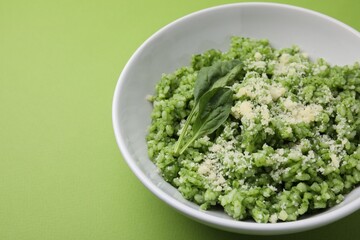 Delicious spinach risotto with parmesan cheese on light green background, closeup. Space for text