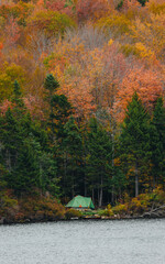 Fototapeta premium Green Tent Camping Side of Lake Autumn in Green Mountains Vermont. Fall Foliage Colorful Trees Canoe On Shore Next to Campsite