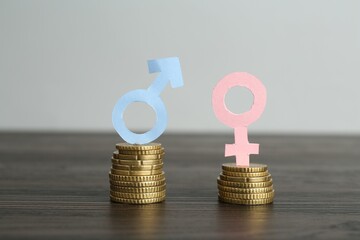 Financial inequality. Male and female symbols with coins on wooden table