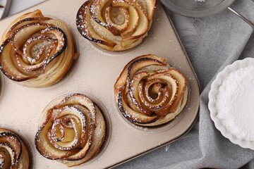 Freshly baked apple roses in cupcake pan on table, closeup. Puff pastry