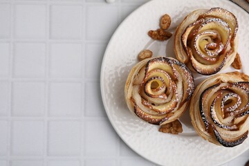 Freshly baked apple roses and walnuts on white tiled table, top view with space for text. Puff pastry