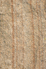 Close up photo of a granulated rock texture. The rock contains tan, reddish browns, and whites with vertical lines. background with copy space.