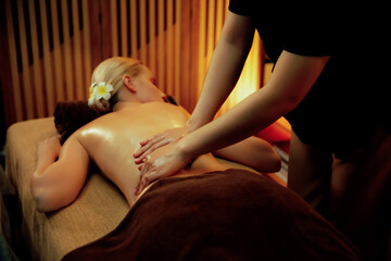 Fototapeta premium Caucasian woman customer enjoying relaxing anti-stress spa massage and pampering with beauty skin recreation leisure in warm candle lighting ambient salon spa at luxury resort or hotel. Quiescent