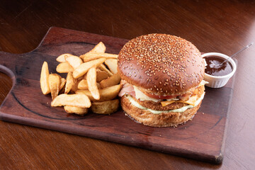 Breaded chicken burger with bacon, lettuce and tomato and top potatoes on a wooden board with bbq sauce