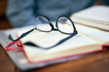 Book, education and glasses on desk in classroom of college or university for development or...
