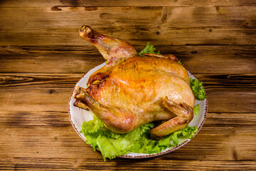 Plate with roasted whole chicken and lettuce leaves on a wooden table