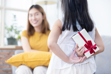 Fototapeta premium Little Girl Hiding Gift Box at Her Back Trying to Surprise Her Mother
