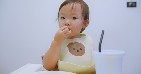 Cute toddler enjoying eating a snack in a high chair wearing a bear-themed bib in a bright and modern kitchen, Perfect for family, childhood, and home lifestyle BLW themes.