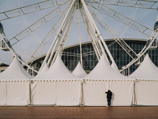 A person looks through the curtain of a event tent next to a ferris wheel