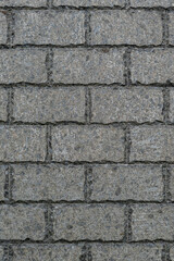 A detailed view of a rough stone wall made up of rectangular, gray granite bricks arranged in a staggered pattern, emphasizing the texture and natural variations of the stone surface.