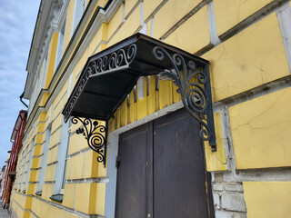 The yellow facade of the house with a forged black visor over the entrance door.