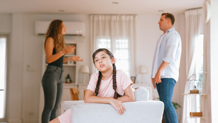 Obraz premium Annoyed and unhappy young girl sitting on sofa trapped in middle of tension by her parent argument in living room. Unhealthy domestic lifestyle and traumatic childhood develop to depression Synchronos