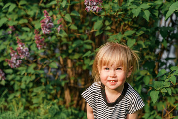 Cute Caucasian toddler child 2-years-old girl walks in a green park at sunset in summer. The concept of a joyful childhood and active pastime.