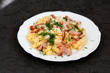 Pasta with beacon, cheese and dill on a white saucer. On a dark abstract background. Home cooking concept. 
