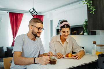 Two friends male and female are eating croissant for breakfast