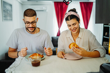 Two friends male and female are eating croissant for breakfast