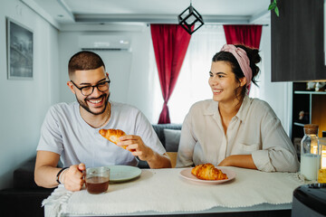 Two friends male and female are eating croissant for breakfast