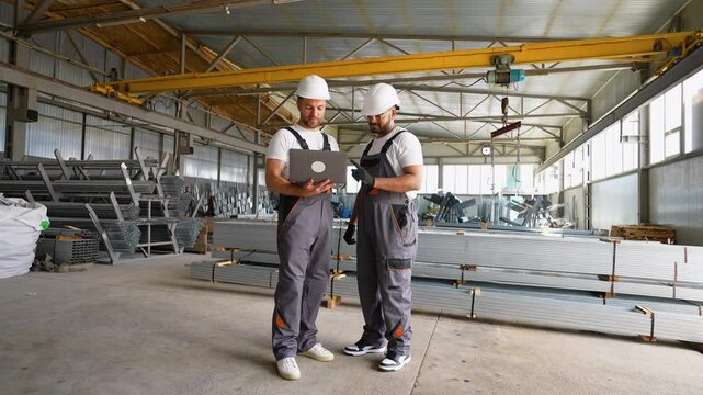 Two diverse workers with laptop in metal profile warehouse