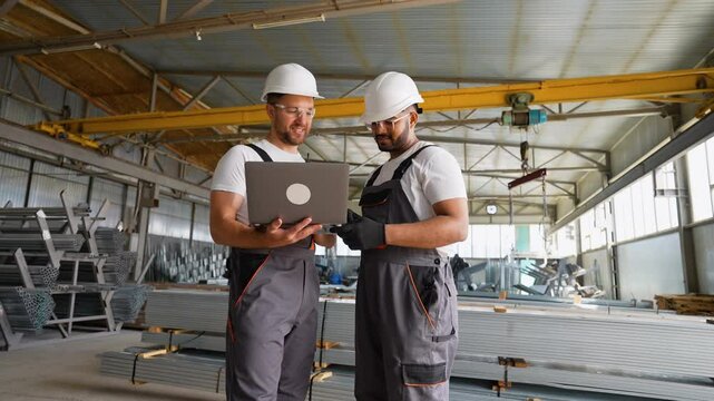 Caucasian foreman and Indian worker with laptop in metal profile warehouse