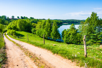Rural road along green fields and meadows and lake view, Suwalski Landscape Park, Podlasie, Poland
