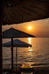 Spectacular sunset on the sea. Greece, Neos Marmaras. The sandy beach in anticipation of the tourist season, Greece. Close up Thatch umbrella and beach chair on tropical beach at summer day.