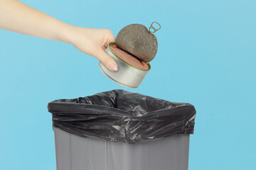 throw canned food in the trash, metal tin can in hand in front of trash can, concept of spoiled...