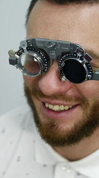 Smiling happy male patient in corrective testing glasses. Checking up eyesight in clinic. Handsome patient in ophthalmology. Vertical video