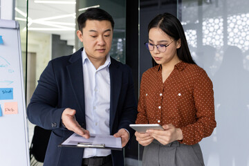 Asian business professionals engaged in discussion, focusing on project details. Man pointing to...