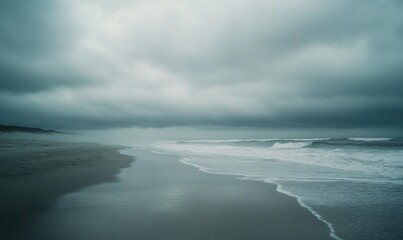 Thick, gray clouds moving slowly across the sky, casting shadows over a deserted beach