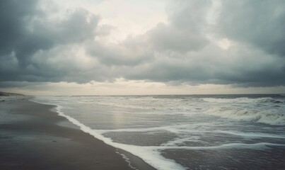 Thick, gray clouds moving slowly across the sky, casting shadows over a deserted beach
