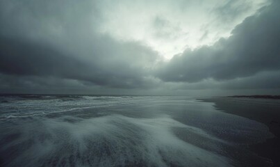 Obraz premium Thick, gray clouds moving slowly across the sky, casting shadows over a deserted beach