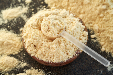 Vanilla flavored whey protein powder in a plastic measuring spoon in a bowl