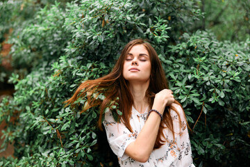 Beautiful young woman standing in front of lush green bushes with hair blowing in the wind