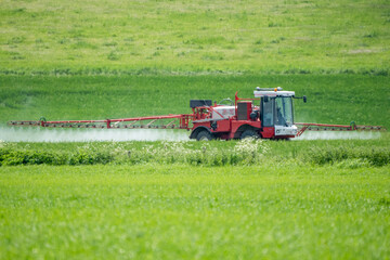 a large red crop sprayer in action in a field of young wheat