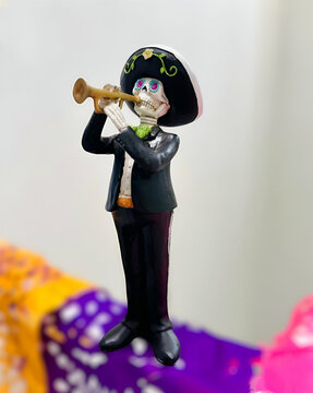 Figura decorativa de una calavera vestida como mariachi, tocando su trompeta, podemos observar que esta sobre papel picado que se utiliza para decorar la famosa ofrenda de d&iacute;a de muertos mexicana.
