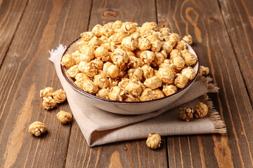 Bowl with crispy popcorn on wooden background