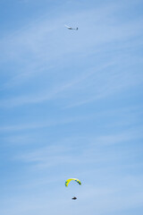 A glider plane soaring through the sky with clouds in the background. down below a paraglider is flying.