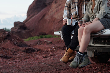 Cropped shot of young restful couple with metallic mugs having tea in the evening while sitting on body of pickup truck
