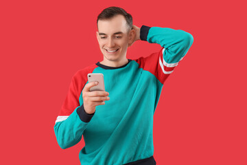 Young man with mobile phone messaging on red background