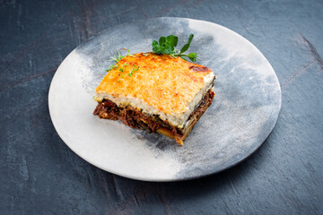 Traditional Greek moussaka with beef mince, eggplant and bechamel sauce served as close-up on a Nordic design plate on a stone board