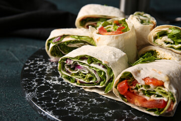 Board of tasty lavash rolls with vegetables and greens on black background