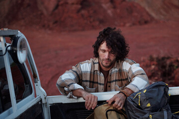 Young man in flannel zipping on unzipping backpack in body of pickup truck while standing in front of vehicle in natural environment © pressmaster