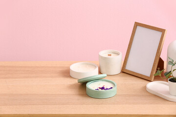 Holders with candles and blank frame on table near pink wall in room