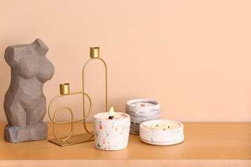 Holders with burning candles and decor on table near beige wall in room