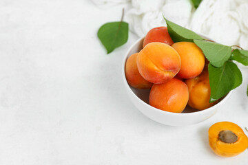 Bowl with fresh apricots and leaves on white background