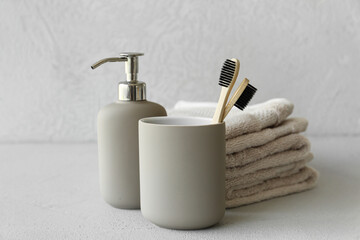 Bamboo tooth brushes in holder, liquid soap and towels on grey background