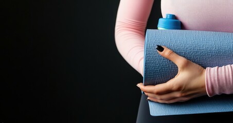 A woman prepares for her workout by holding a pink yoga mat and a blue water bottle, dressed in sportswear and focused on her fitness training routine