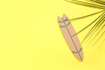 Mini surfboard with palm leaf on yellow background