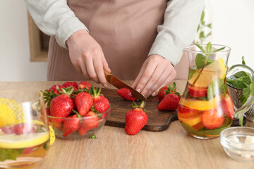 Woman cutting strawberry for lemonade in kitchen